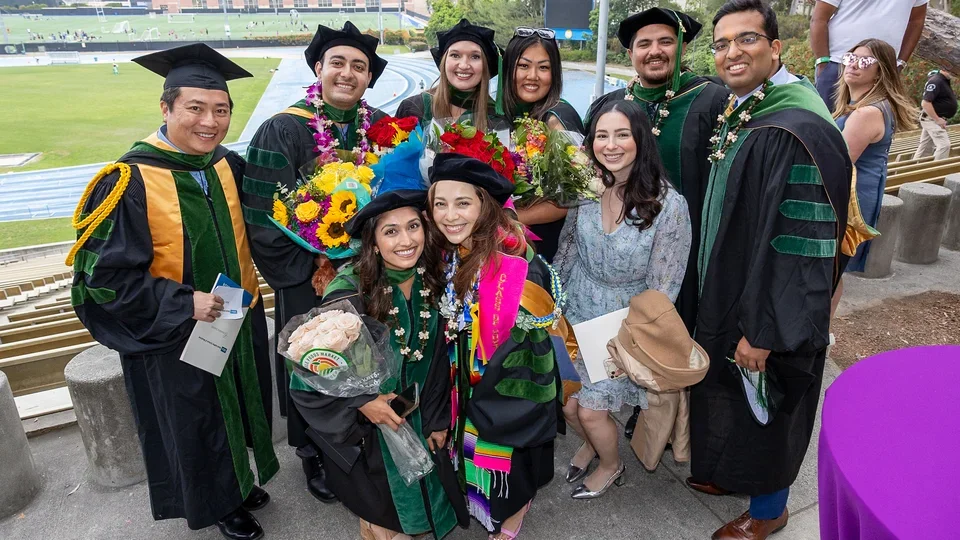 A group of graduates in caps and gowns smiling together at DGSOM Commencement ceremony, celebrating their achievements.