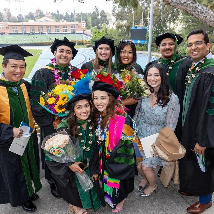 A group of graduates in caps and gowns smiling together at DGSOM Commencement ceremony, celebrating their achievements.