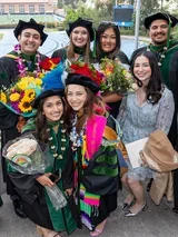 A group of graduates in caps and gowns smiling together at DGSOM Commencement ceremony, celebrating their achievements.
