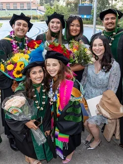 A group of graduates in caps and gowns smiling together at DGSOM Commencement ceremony, celebrating their achievements.
