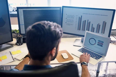 Male sitting a desk in front of laptop and multiple monitors