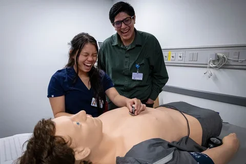 A cheerful scene featuring two individuals smiling at a mannequin, highlighting their enjoyment and engagement with the mannequin. simulating a medical exam.