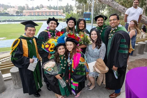 A group of graduates in caps and gowns smiling together at DGSOM Commencement ceremony, celebrating their achievements.