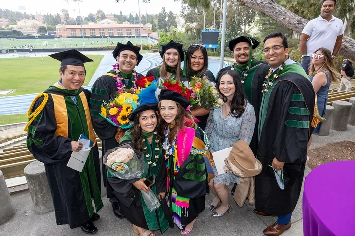 A group of graduates in caps and gowns smiling together at DGSOM Commencement ceremony, celebrating their achievements.