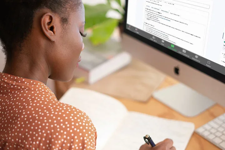 Person sitting at a computer with notebook and zoom meeting displaying on the computer