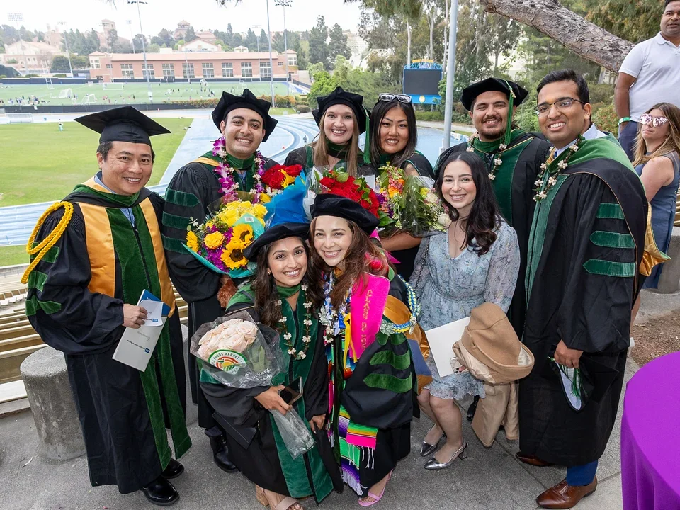 A group of graduates in caps and gowns smiling together at DGSOM Commencement ceremony, celebrating their achievements.