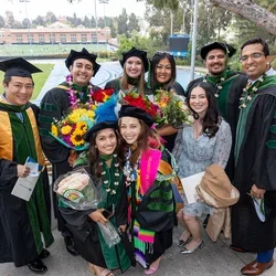 A group of graduates in caps and gowns smiling together at DGSOM Commencement ceremony, celebrating their achievements.