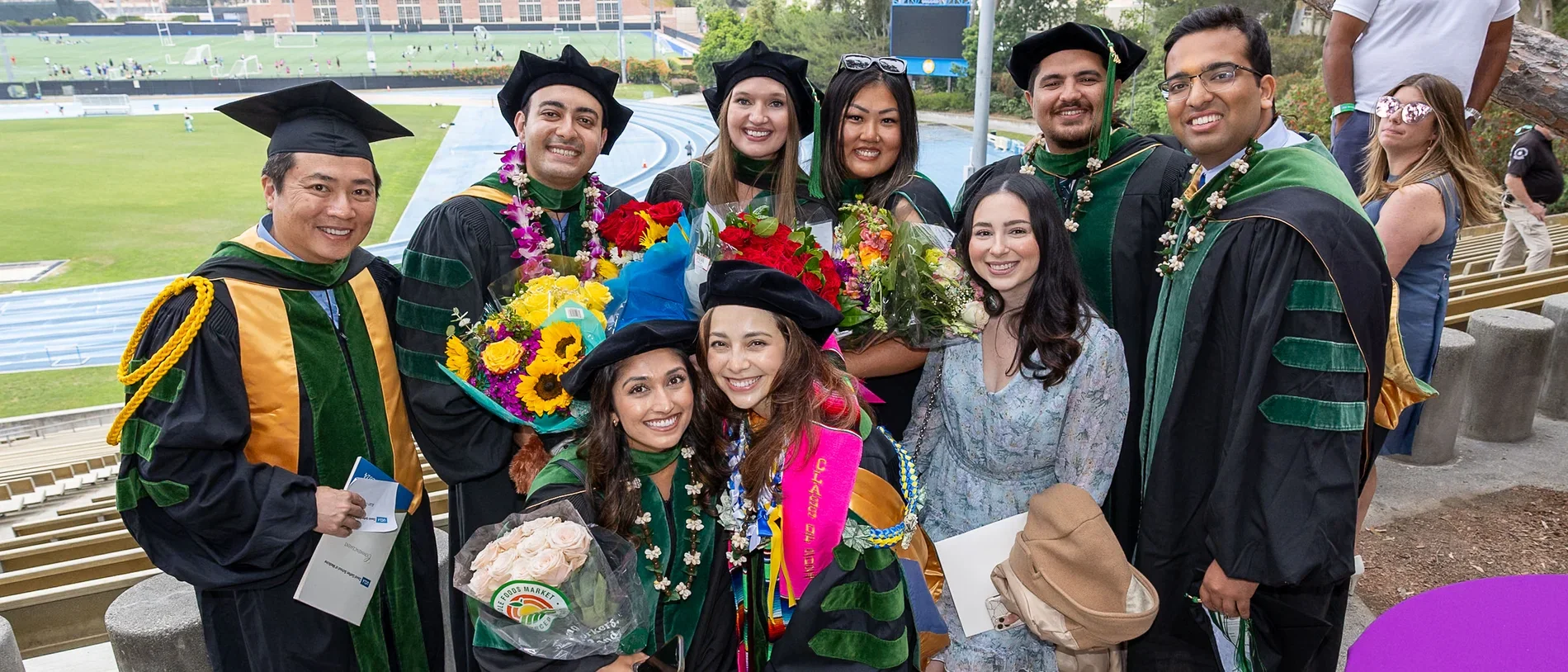 A group of graduates in caps and gowns smiling together at DGSOM Commencement ceremony, celebrating their achievements.